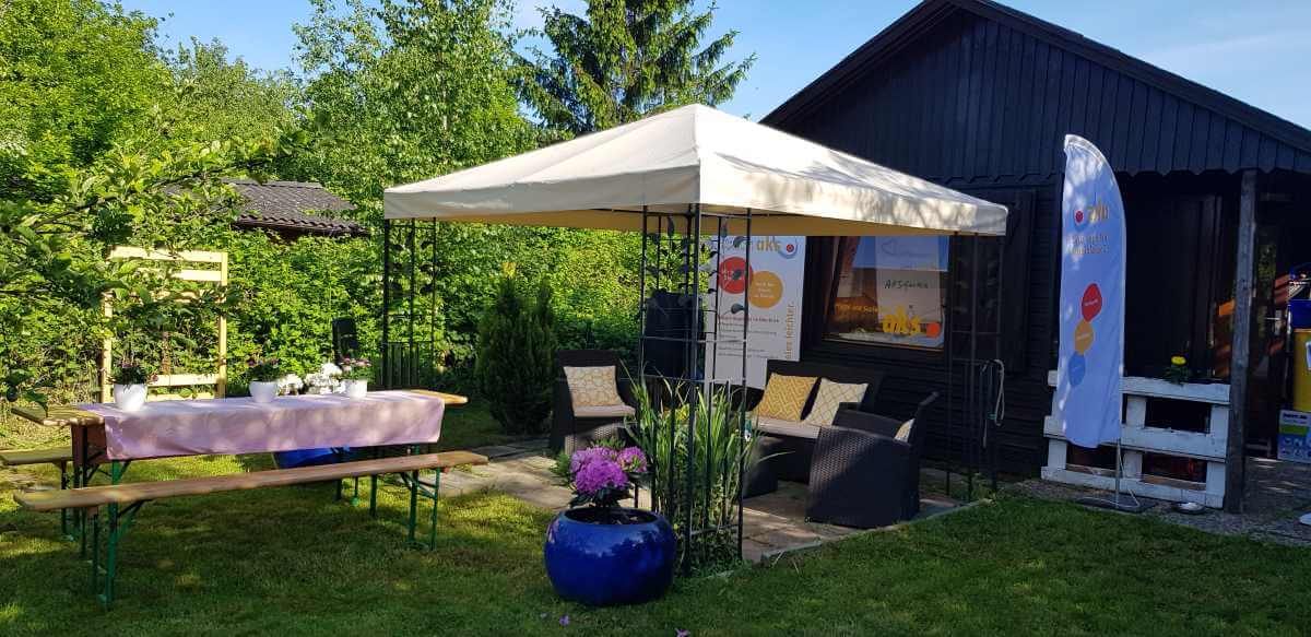 Garden with gazebo, seating, a blue flower pot, and a black garden shed in the background
