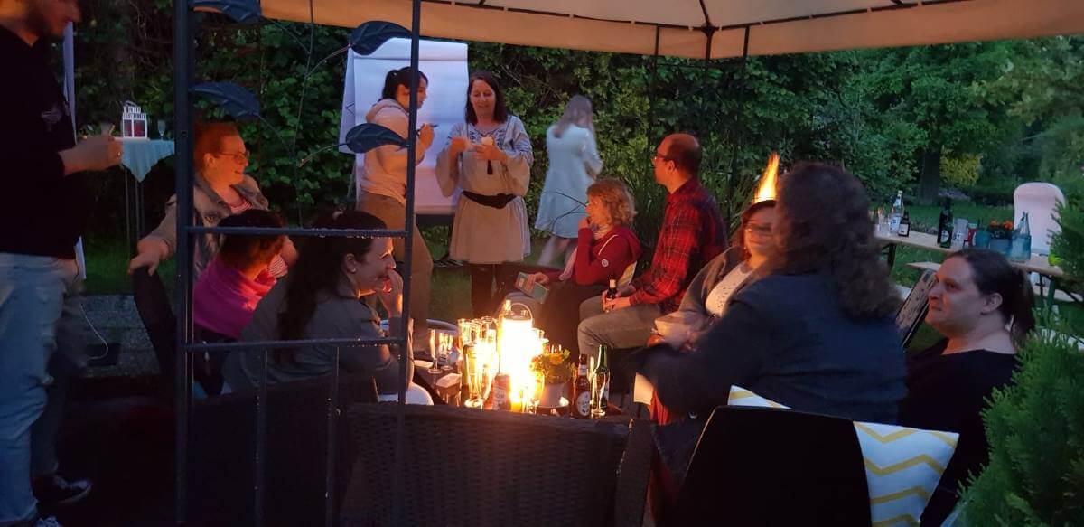 Group of people sitting under a parasol in the garden in the evening around a table with candles and drinks