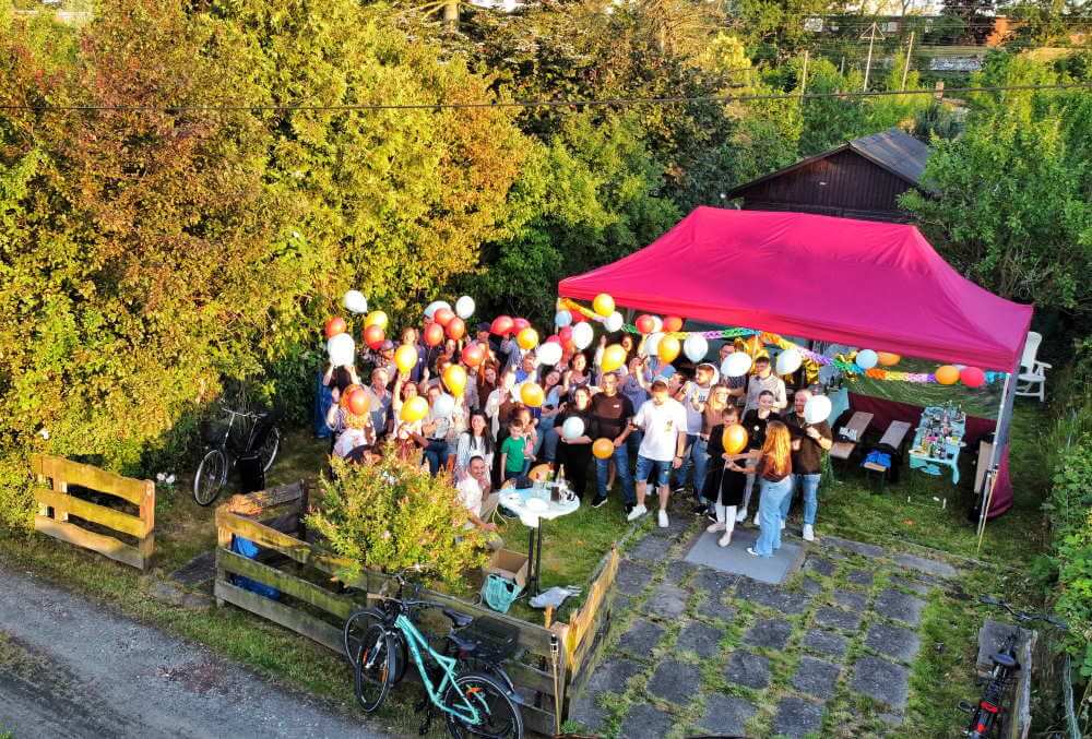 Group of people with balloons under a red gazebo in a garden with bicycles and trees